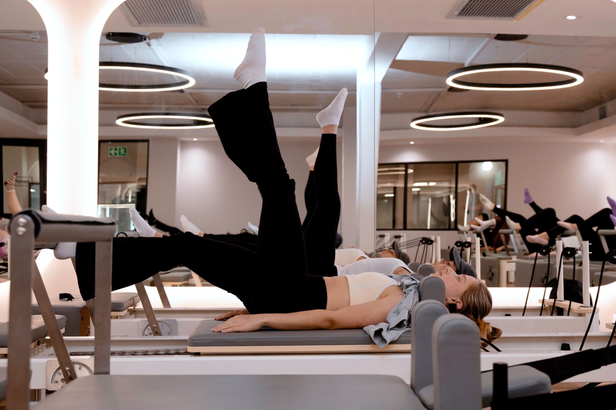 Women lifting their legs high on the reformers, mirrors and ring lights behind them